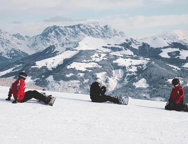 Snowboarderin sitzt lachend im Schnee mit erhobenem Arm.