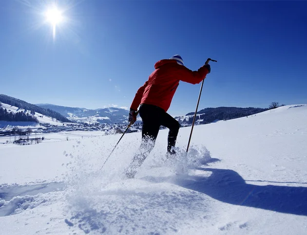 Langläufer in roter Jacke auf sonniger Schneelandschaft mit Bergen im Hintergrund