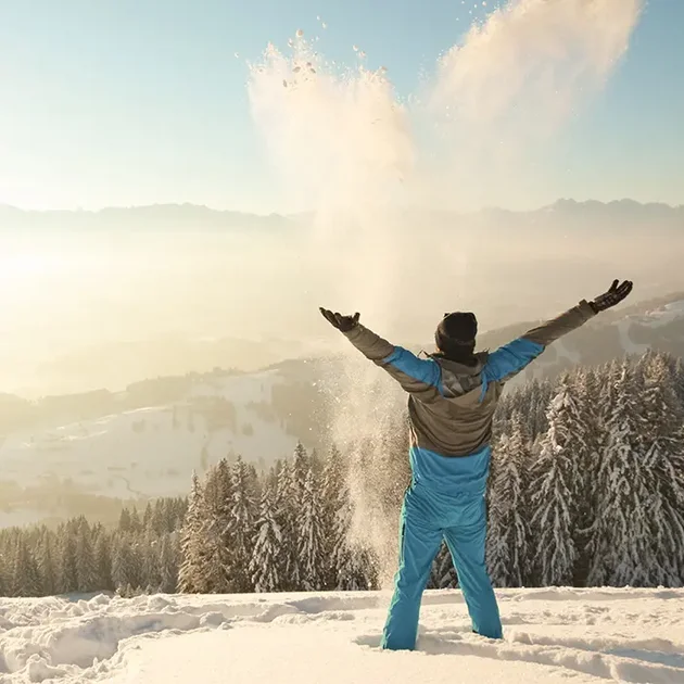 Mann steht im Schnee und streckt Hände in die Höhe im Allgäu