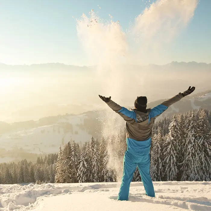 Mann steht im Schnee und streckt Hände in die Höhe im Allgäu