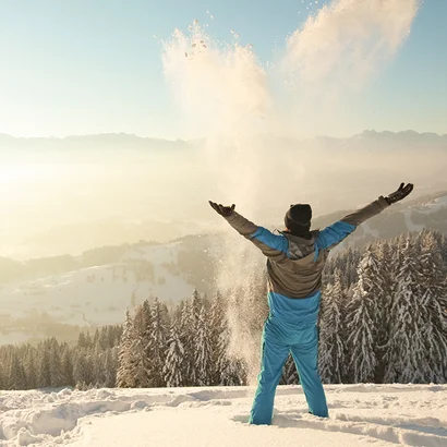 Mann steht im Schnee und streckt Hände in die Höhe im Allgäu