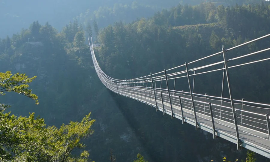 Spektakuläre Hängebrücke spannt sich über eine bewaldete Schlucht, von der Sonne angestrahlt.