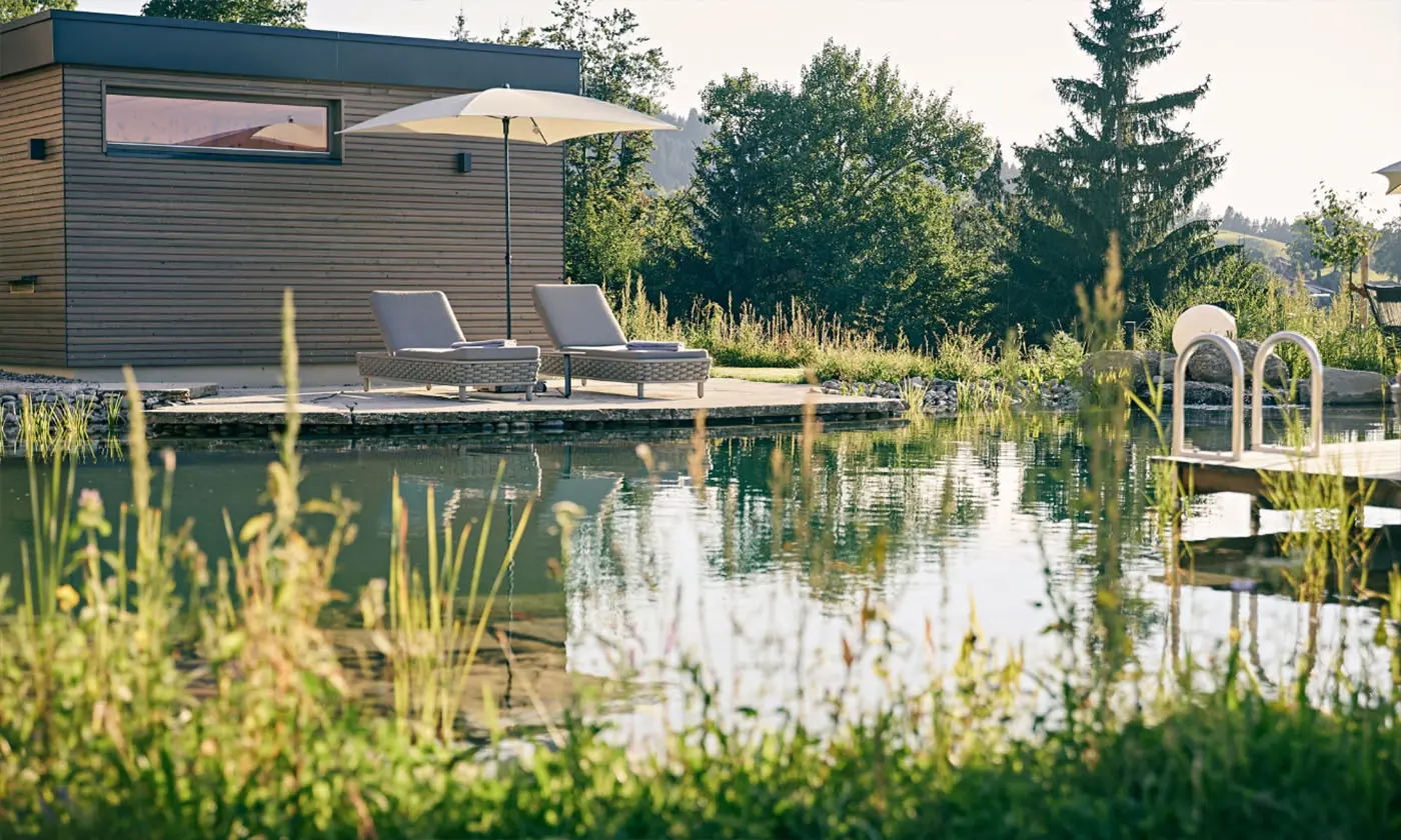 Zwei Liegen mit Sonnenschirm am Holzdeck neben dem Birkenhof-Naturteich.