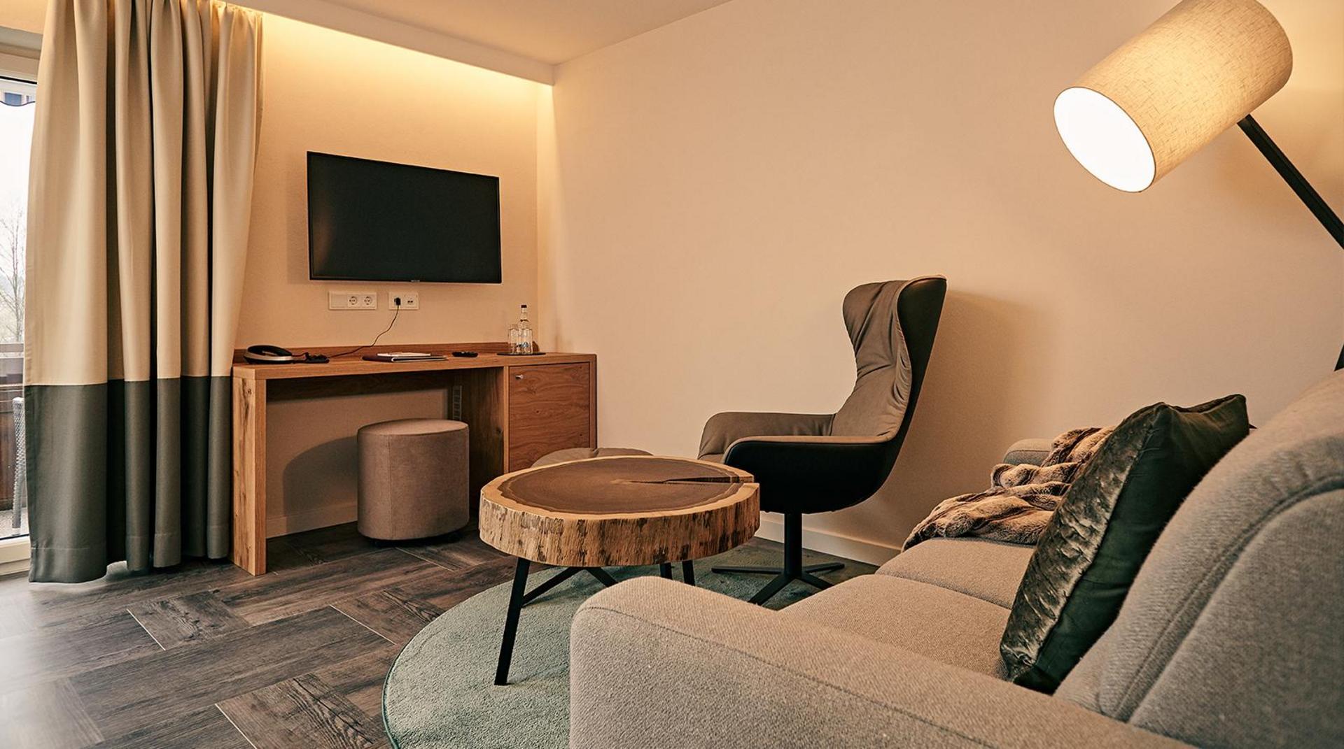Wohnbereich mit Sofa, Sessel, Schreibtisch und TV an der Wand.
