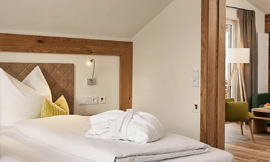 Komfortables Schlafzimmer mit weißer Bettwäsche, Holzrahmen und einem bereitliegenden Bademantel
