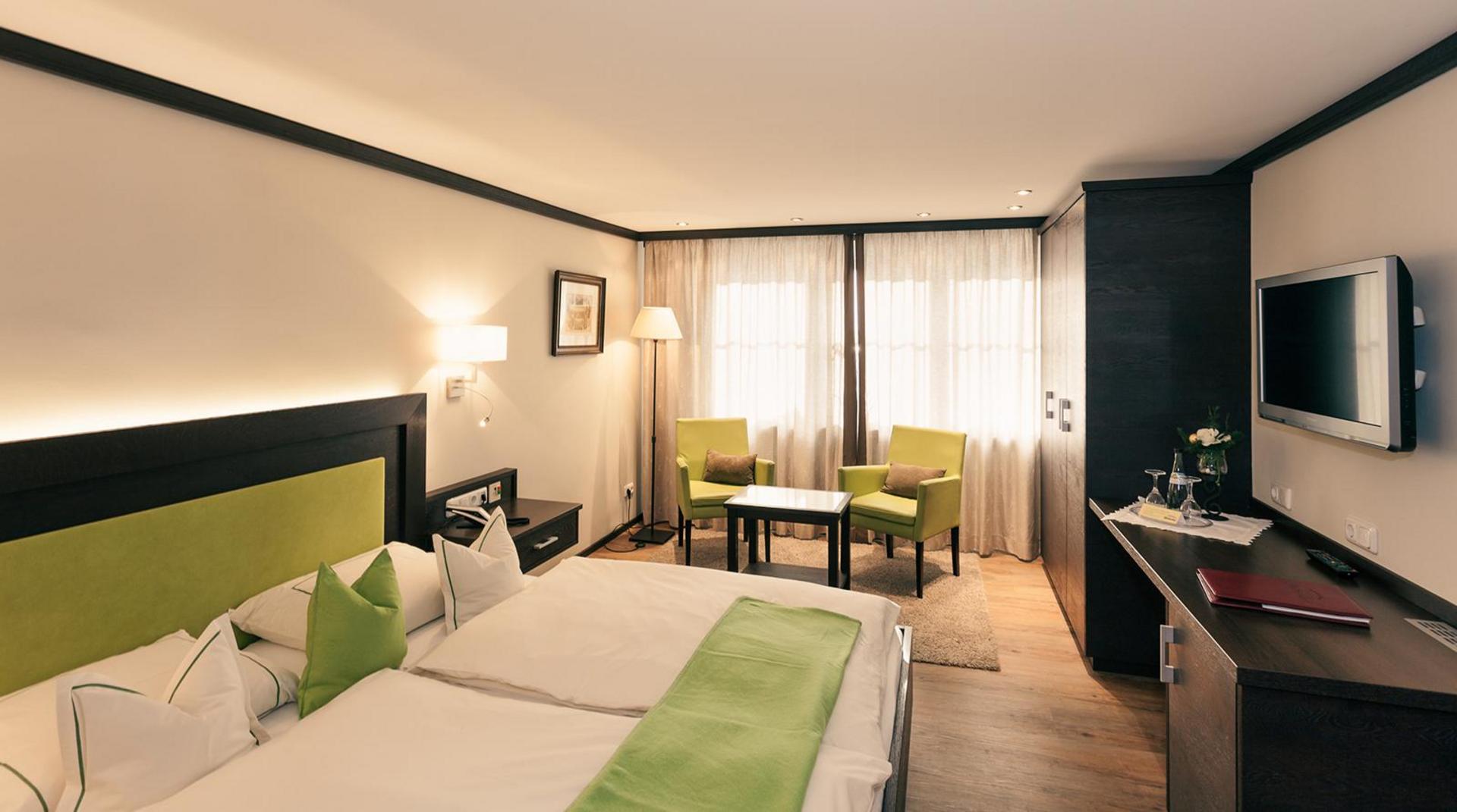 Großzügiges Doppelzimmer mit grünen Akzenten, Sitzgruppe und Balkonblick.