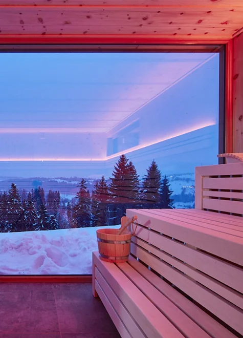 Panorama-Sauna mit großem Fenster und Blick in die verschneite Winterlandschaft.