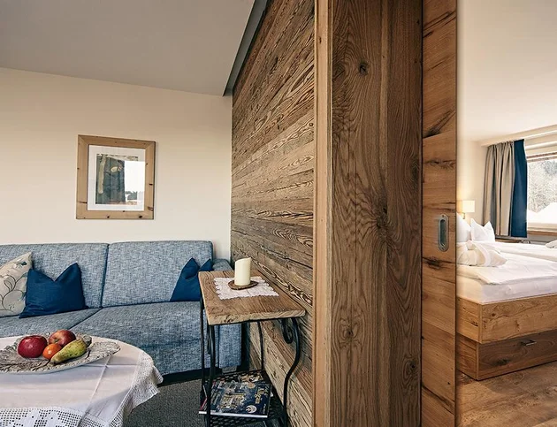 Wohnzimmerbereich mit blauer Couch, Obstteller und Blick ins angrenzende Schlafzimmer
