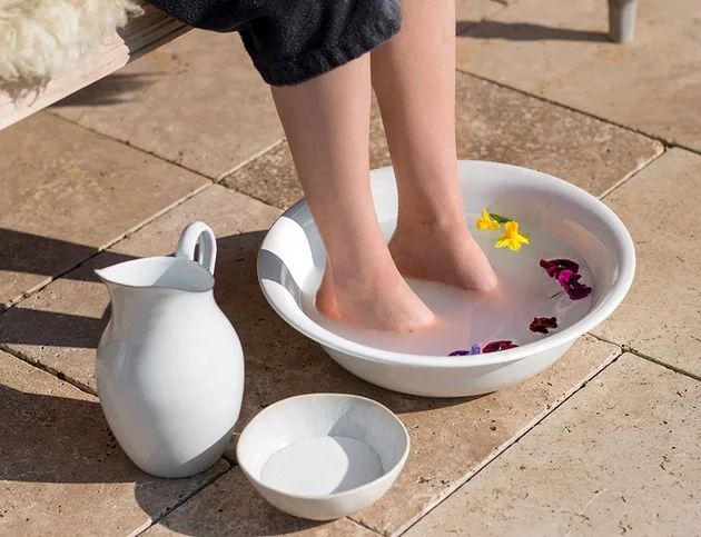 Fußbad mit Blüten im Rahmen der Basenfasten-Kur im Hotel Birkenhof Oberstaufen – weiße Schale, Kanne und Schälchen auf Natursteinboden.