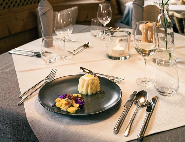 Festlich gedeckter Tisch mit Dessert und essbaren Blüten auf schwarzem Teller.