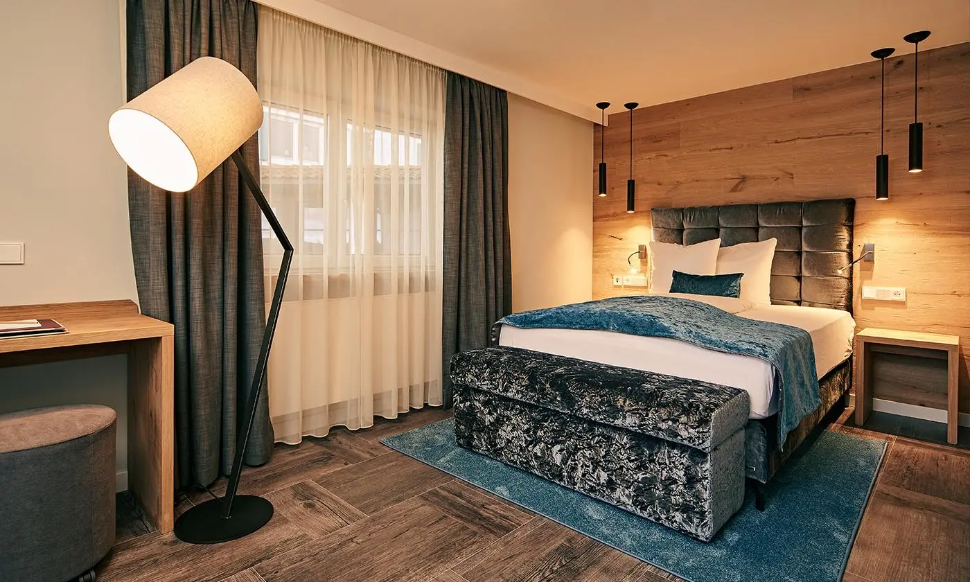 Modernes Hotelzimmer mit großem Bett, blauen Akzenten, Holzwand und Stehlampe