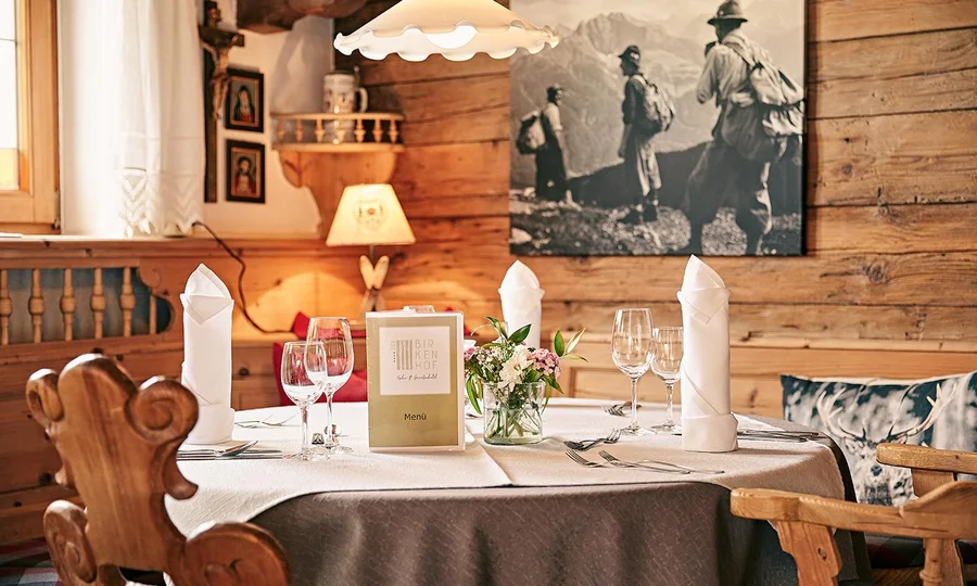 Elegant gedeckter Tisch im urigen Restaurant mit weißem Tischtuch, Gläsern, Servietten und Holzwänden