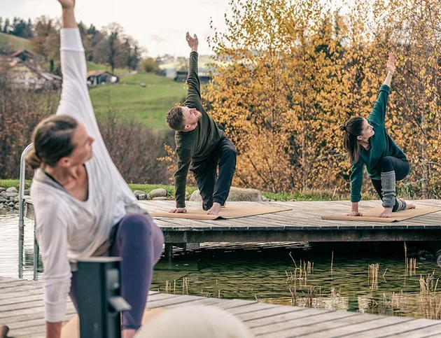 Gruppe macht Yogaübungen auf Holzplattform am Naturteich.