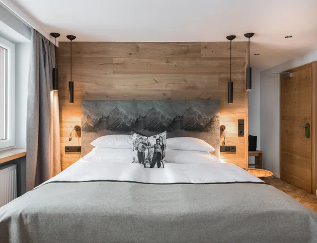 Doppelzimmer „Hochgrat“ mit großem Bett, Holzwand und stilvollen Lampen.