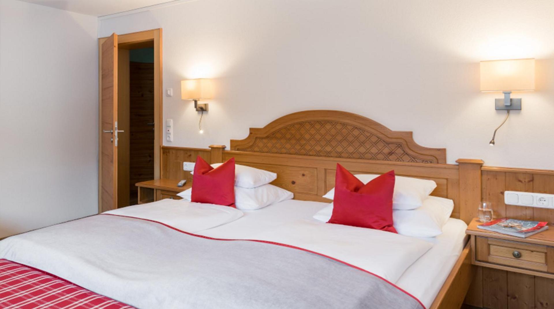 Doppelzimmer mit Holzvertäfelung, roter Bettdeko und Nachttischen.