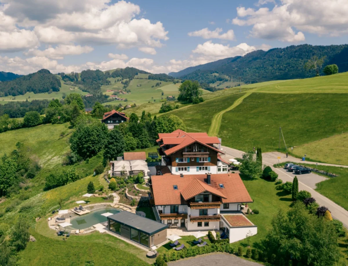 Hotelanlage inmitten grüner Hügel mit Pool – Luftaufnahme eines Hotels mit roten Dächern, Pool und umliegender Berglandschaft.