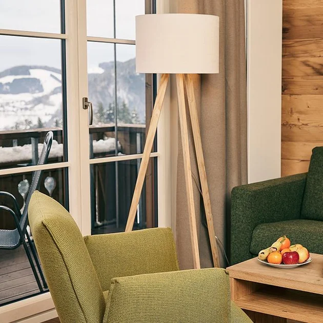 Wohnbereich im Hotel Birkenhof Oberstaufen mit grünem Sessel, Stehlampe, Couchtisch mit Obstschale und Blick auf die verschneiten Allgäuer Berge durch die Fenster.
