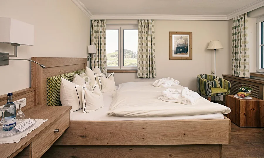 Helles Doppelzimmer mit Holzdesign, weißen Bettwaren und Blick durch das Fenster