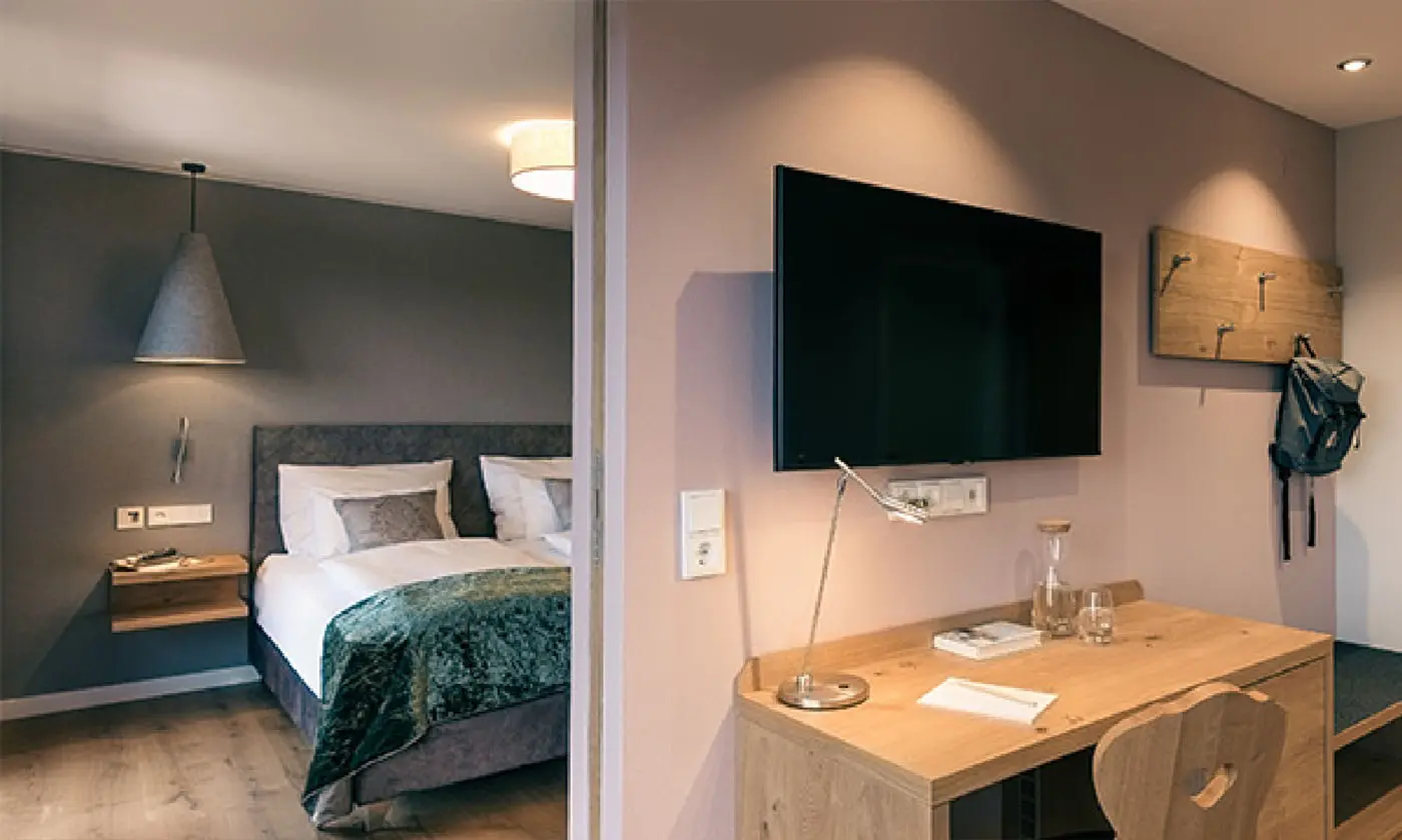 Bedroom with grey wall, large double bed and desk with TV in the Hotel Birkenhof Oberstaufen.