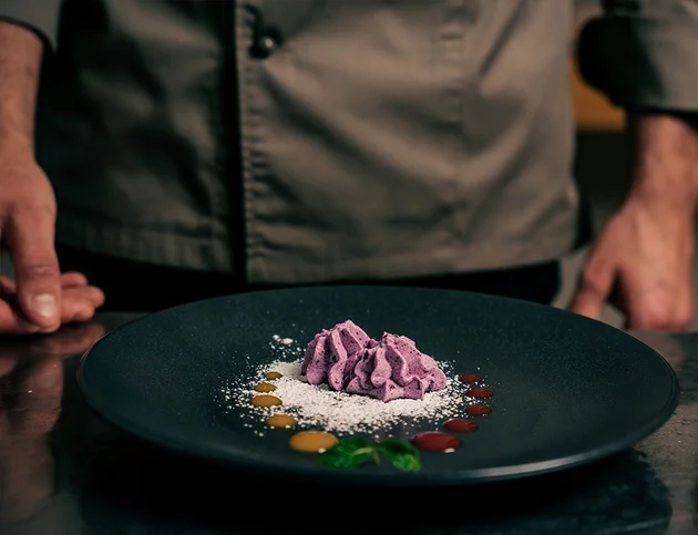 Schwarzer Teller mit violettem Dessert, garniert mit Puderzucker und Soßen.