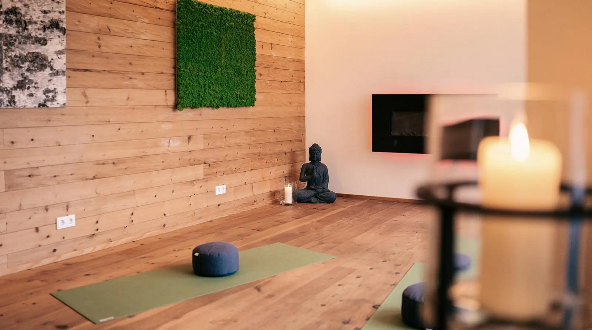 Yogaraum im Hotel Birkenhof Oberstaufen mit Yogamatten, Meditationskissen, Buddha-Figur und modernem Kamin auf Holzfußboden.