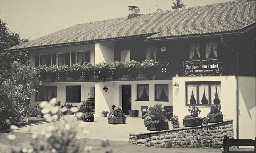 Historische Schwarz-Weiß-Aufnahme des ursprünglichen Landhauses Birkenhof mit Blumenschmuck und klassischer Fassadengestaltung.