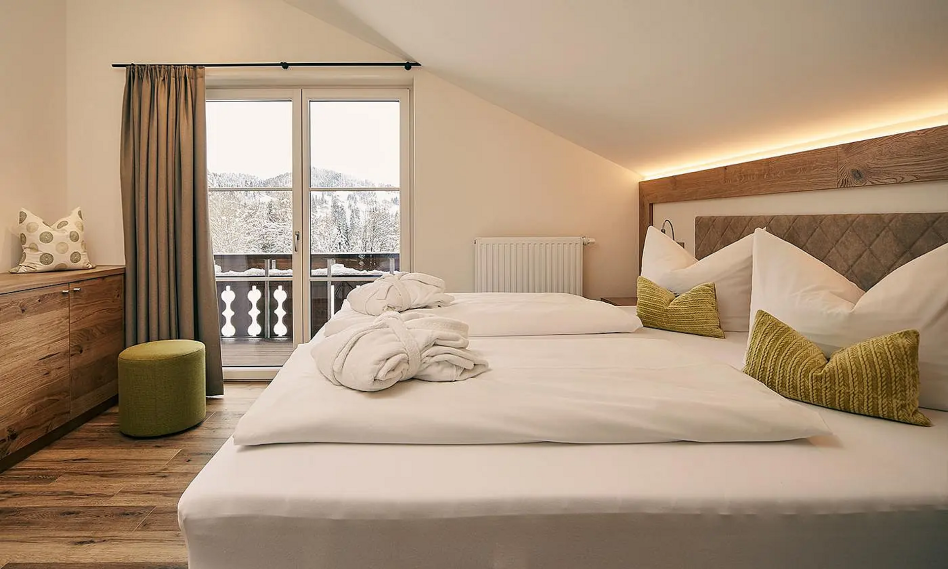 Gemütliches Doppelzimmer mit Holzboden, großen Kissen, Bademänteln und Zugang zum Balkon