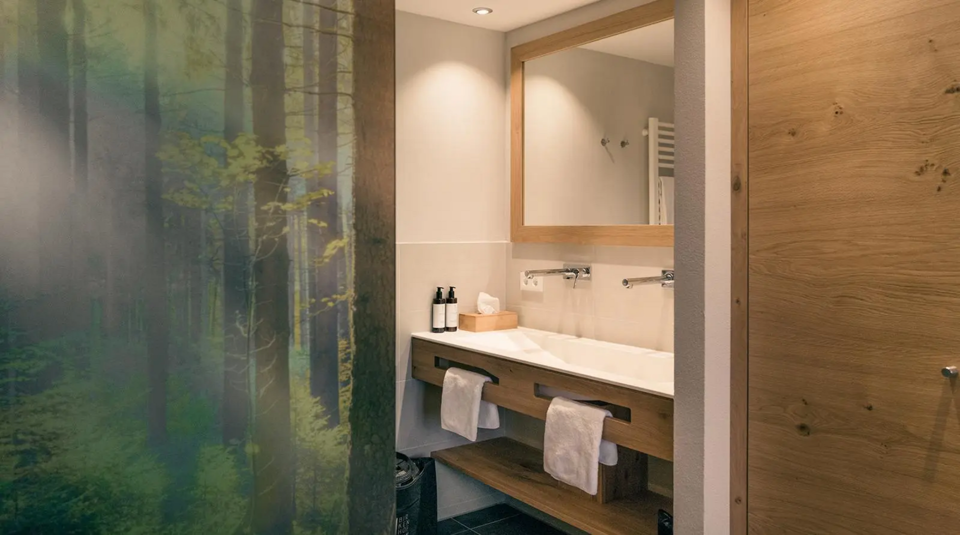 Modernes Badezimmer mit großem Spiegel, Doppelwaschtisch aus Holz und Glaswand mit Waldmotiv.