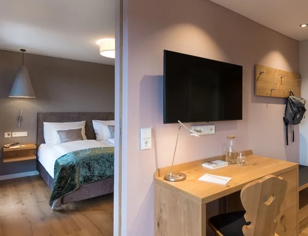 Arbeitsbereich mit Schreibtisch, Fernseher und Blick ins Schlafzimmer mit Doppelbett