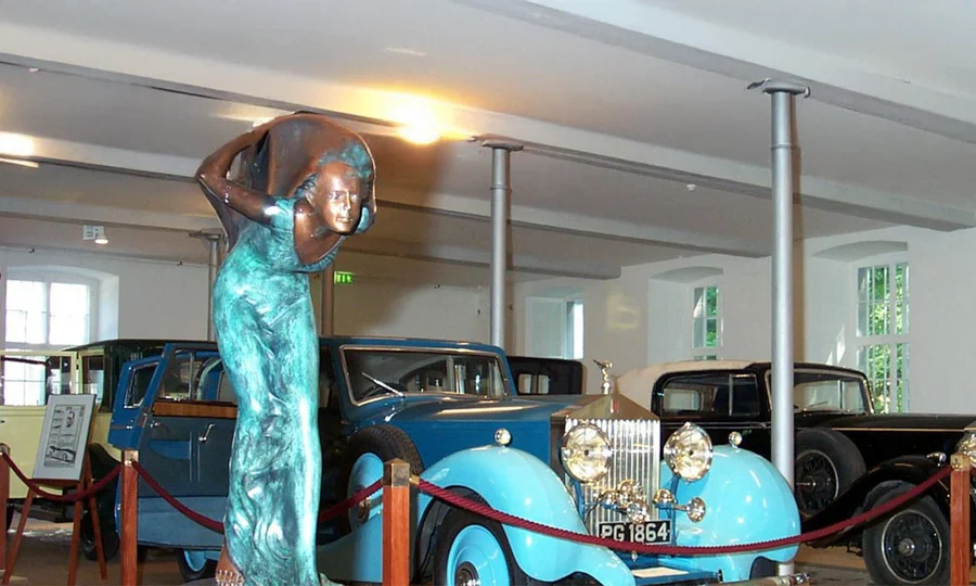 Oldtimer-Ausstellung mit blauen klassischen Autos und einer Bronzestatue im Rolls-Royce Museum in Dornbirn