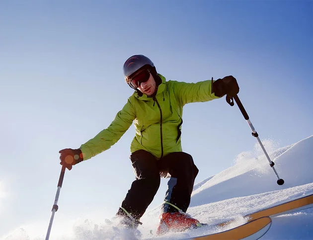 Skifahrer in grüner Jacke fährt schwungvoll einen Hang hinunter.