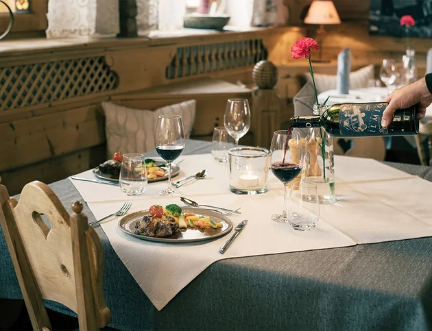 Festlich gedeckter Tisch mit Hauptgerichten und einer Hand, die Rotwein einschenkt.