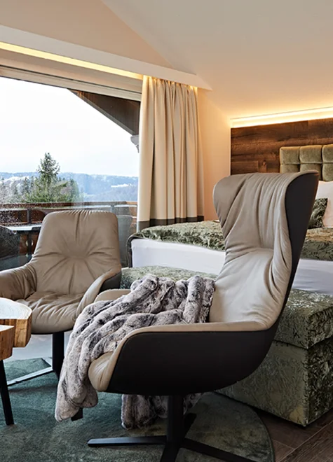 Schlafzimmer mit zwei bequemen Sesseln, Doppelbett und Blick nach draußen.