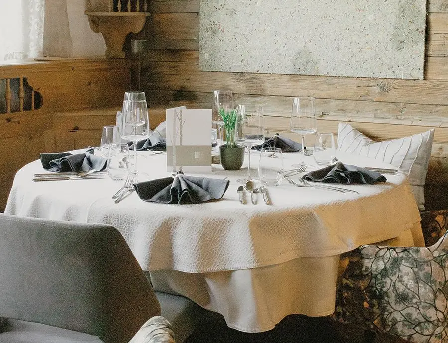 Rund gedeckter Tisch mit weißen Tischdecken, schwarzen Servietten und stilvollem Gedeck im Hotel Birkenhof.
