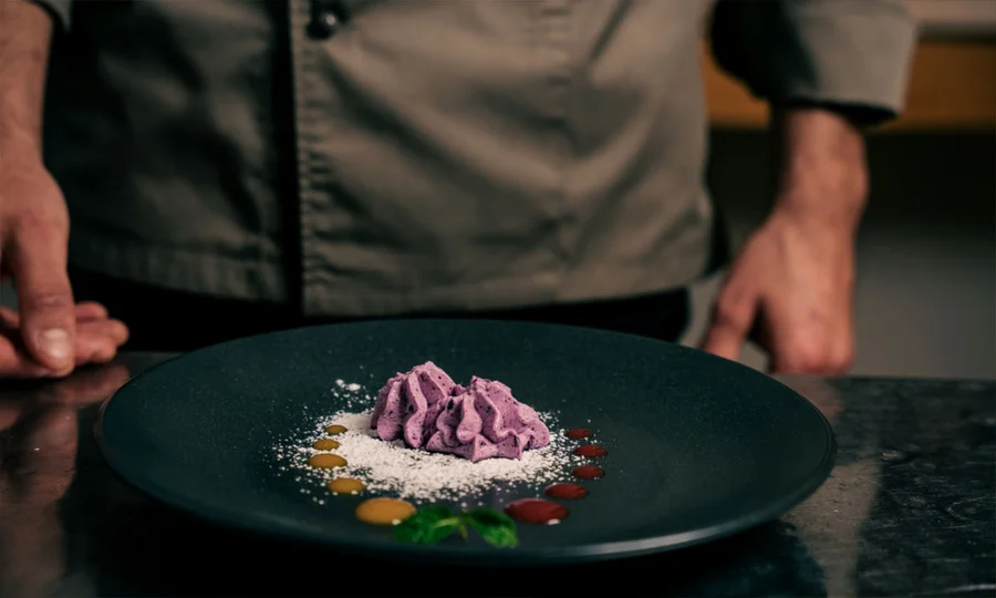 Kreativ angerichtetes Dessert auf schwarzem Teller, serviert von einem Koch