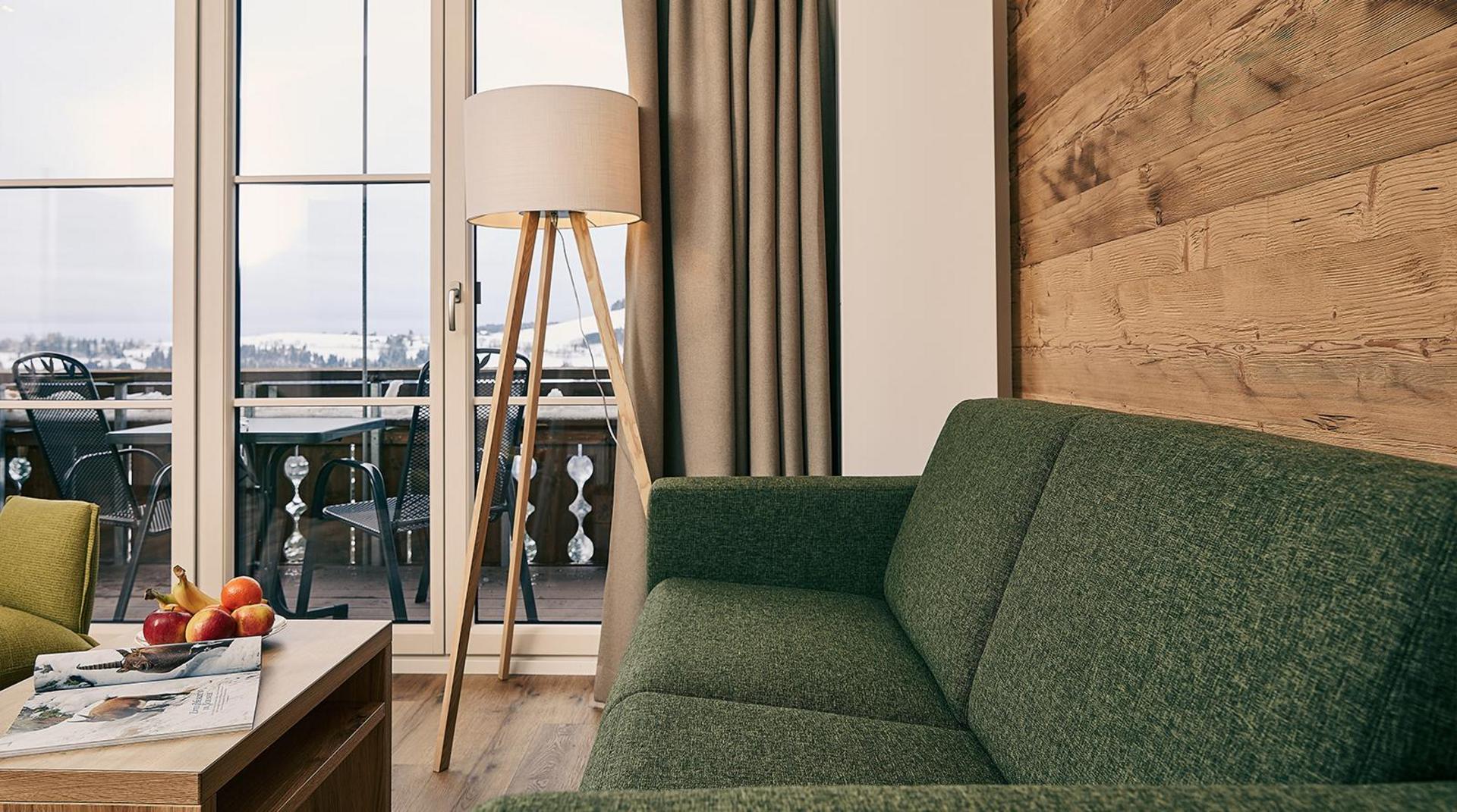 Wohnbereich mit grünem Sofa, Holzvertäfelung und Blick auf den Balkon.