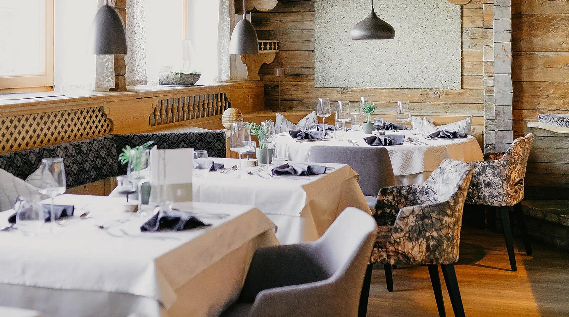 Stube im Hotel Birkenhof Oberstaufen mit eingedeckten Tischen, gemütlicher Holzvertäfelung und stilvollen Polsterstühlen.