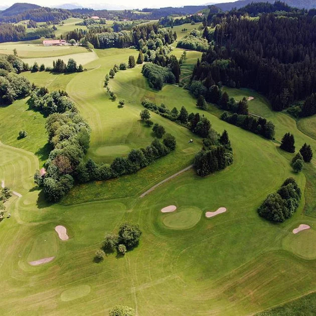 Luftaufnahme eines weitläufigen Golfplatzes im Allgäu, eingebettet in eine grüne Hügellandschaft mit Wäldern und Feldern.