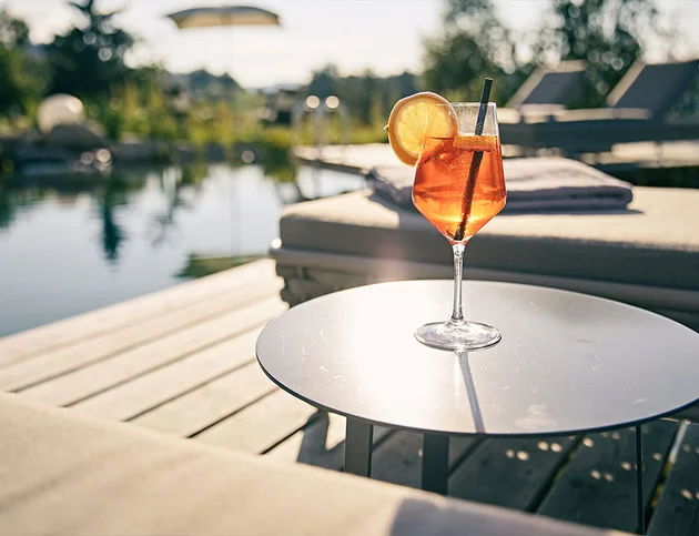 Glas Aperol Spritz mit Orangenscheibe auf einem Tisch am Pool.