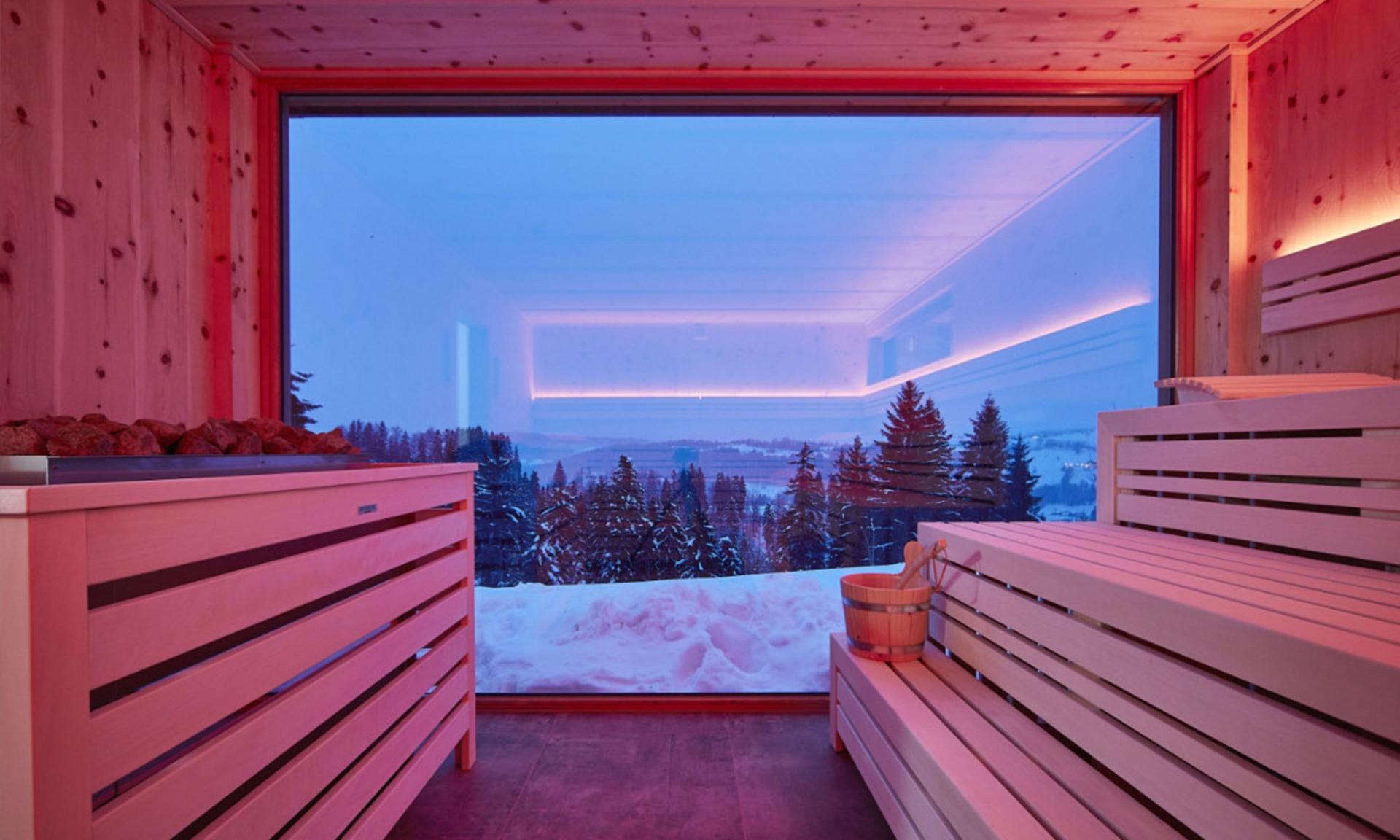 Moderne Panorama-Sauna mit großem Fenster und Blick auf verschneite Landschaft
