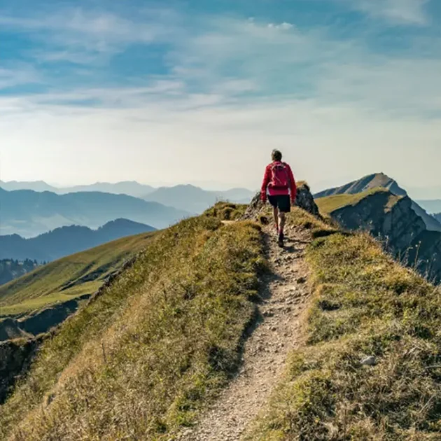 Wanderer auf einem schmalen Bergpfad mit beeindruckendem Alpenpanorama im Allgäu.