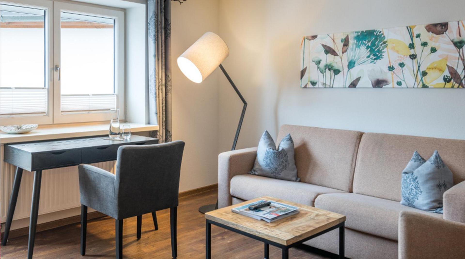 Heller Wohnbereich mit Sofa, Schreibtisch und Blumendekor an der Wand.