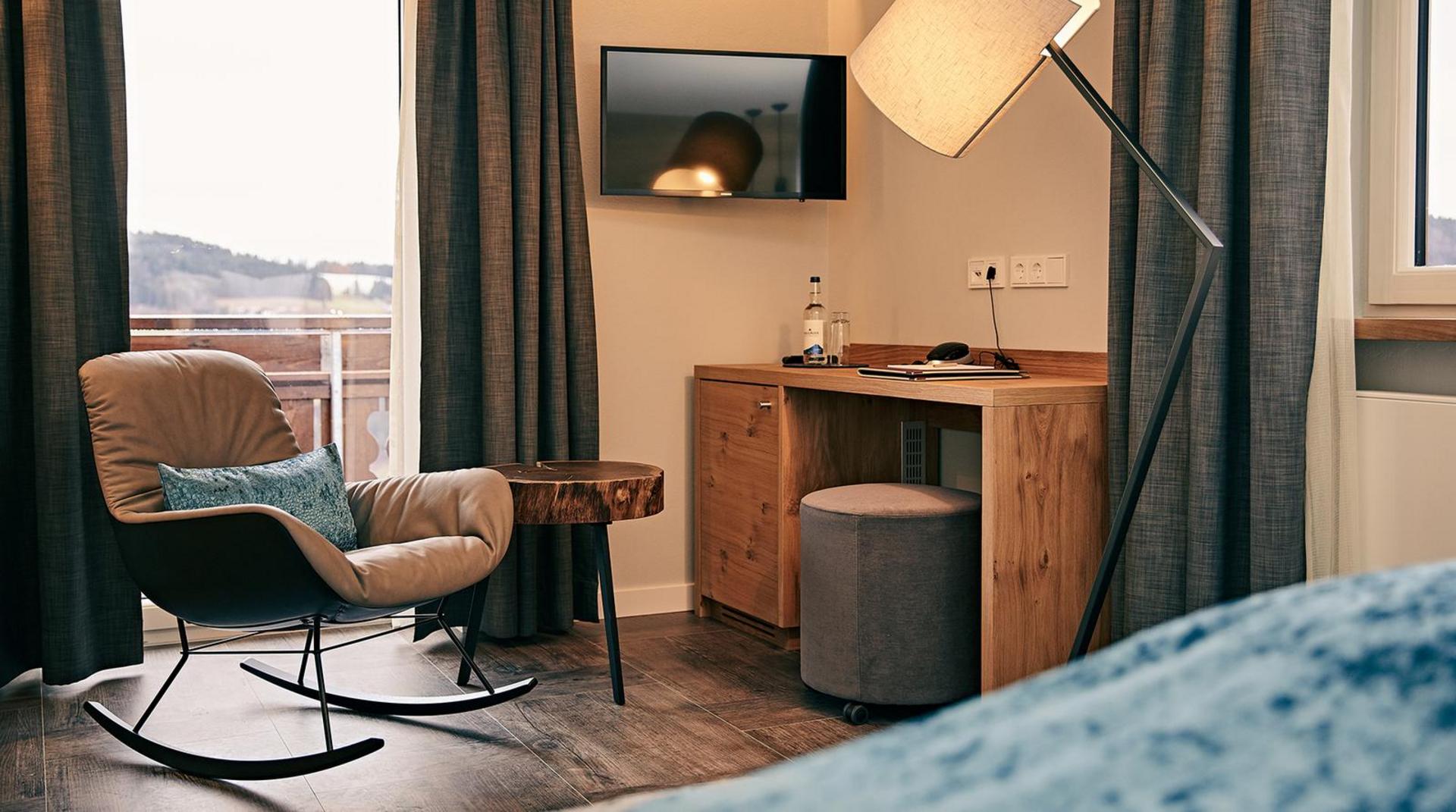 Gemütliche Sitzecke mit Schaukelstuhl, kleinem Holztisch, Schreibtisch mit Hocker, Stehlampe und Balkonblick.