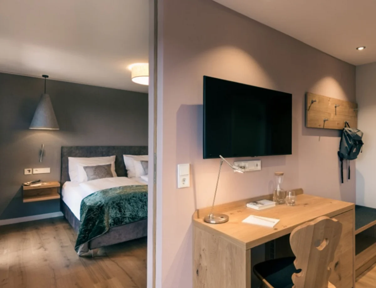 Hotelzimmer mit Schreibtisch und Fernseher – Blick auf Schreibtisch mit Flachbild-TV, im Spiegel ist das Bett zu sehen.