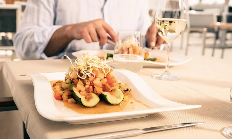 Gefüllte Zucchini mit Gemüsewürfeln, Sprossen und Sauce, dazu Weißwein.