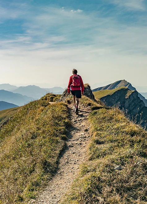 Wanderer auf einem schmalen Grat mit Blick auf die umliegenden Berge im Sommer.
