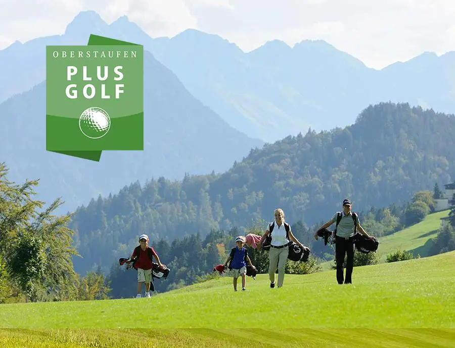 Vier Personen mit Golftaschen gehen über eine grüne Wiese, im Hintergrund Berge und Logo „Oberstaufen PLUS Golf“.