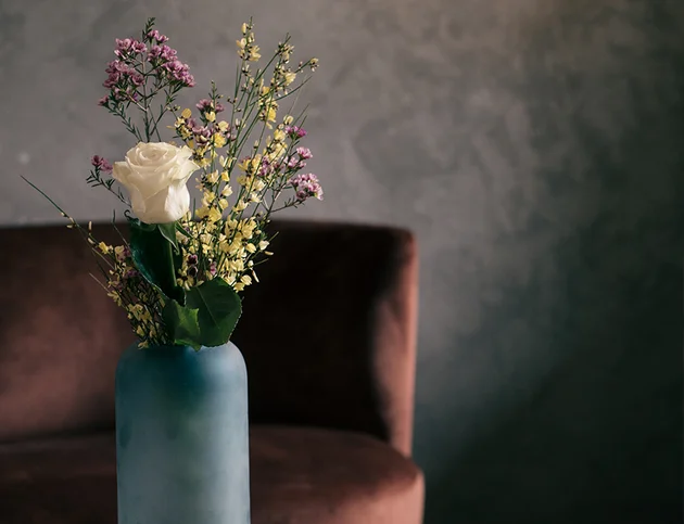 Vase mit weißer Rose und bunten Trockenblumen auf einem Tisch vor dunklem Hintergrund