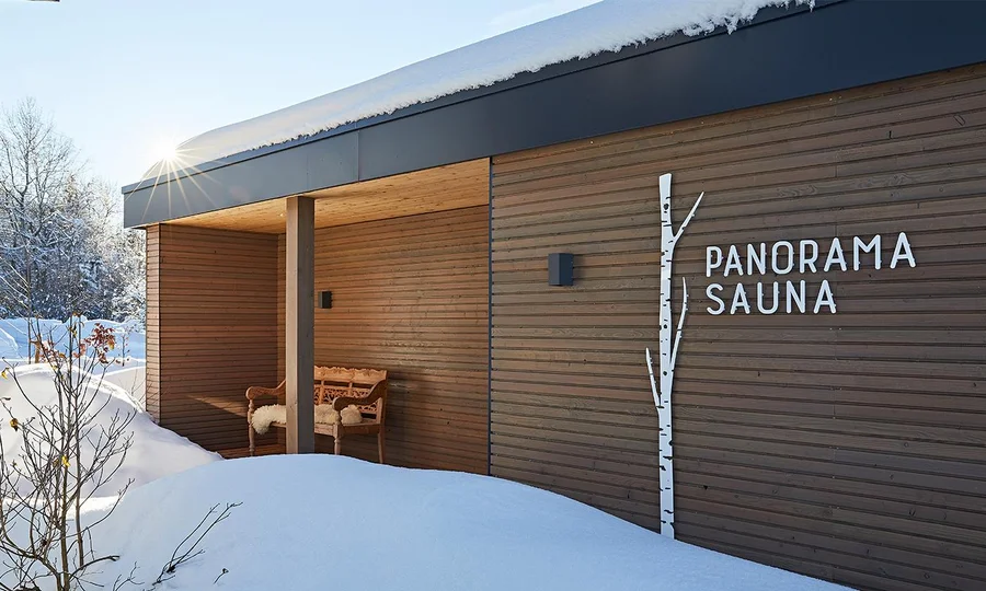 Panoramasauna Winter Hotel Birkenhof Oberstaufen Allgäu Außenansicht einer modernen Holzsauna im Schnee mit der Aufschrift „Panorama Sauna“