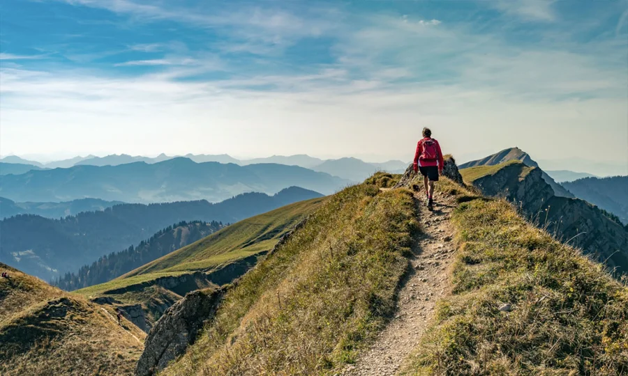 Wanderer auf schmalem Bergkamm mit weitem Blick über die Allgäuer Alpen rund um den Birkenhof.